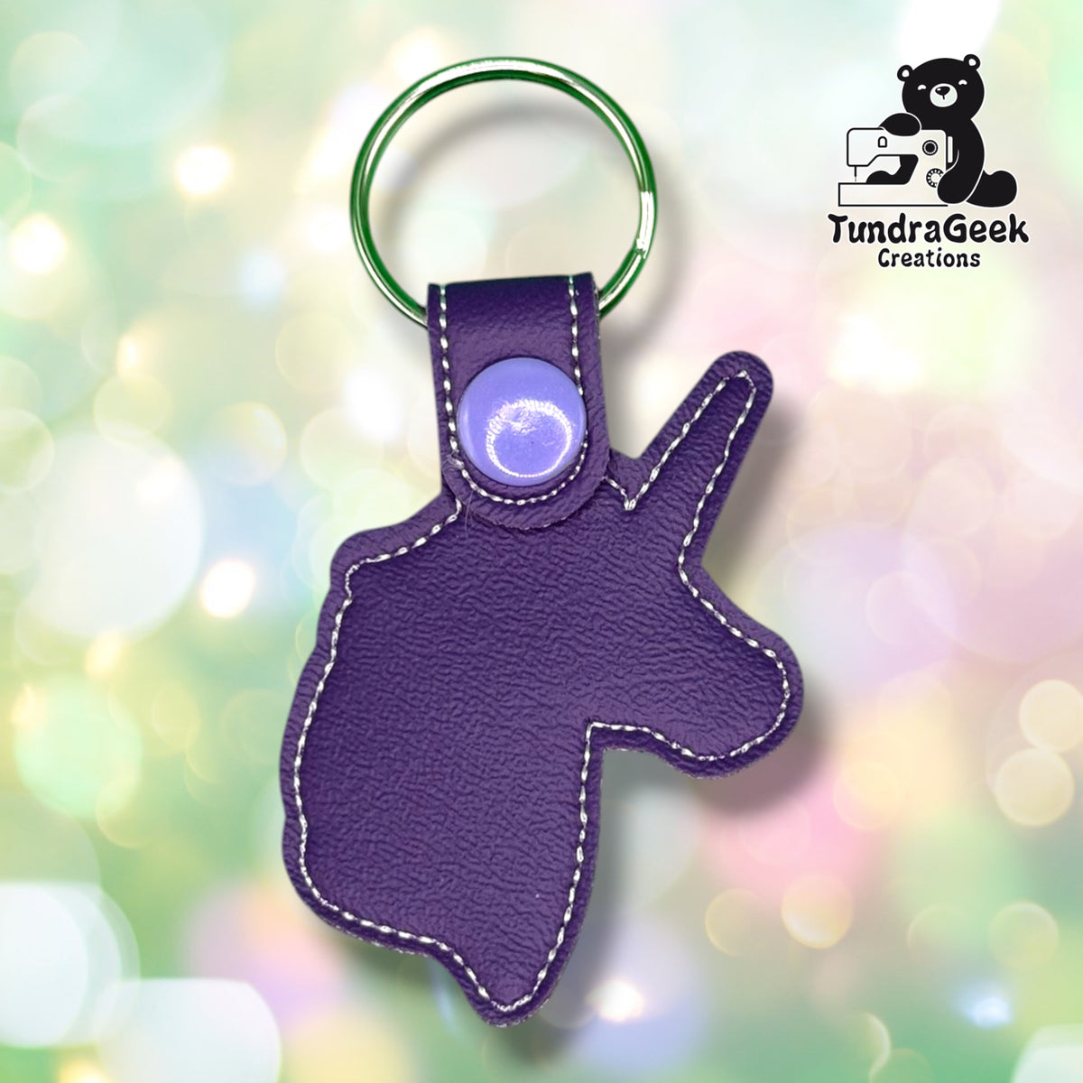 Back view of the keychain showing the plain purple vinyl backing, purple plastic snap closure tab, and split ring. No embroidery visible from this side.