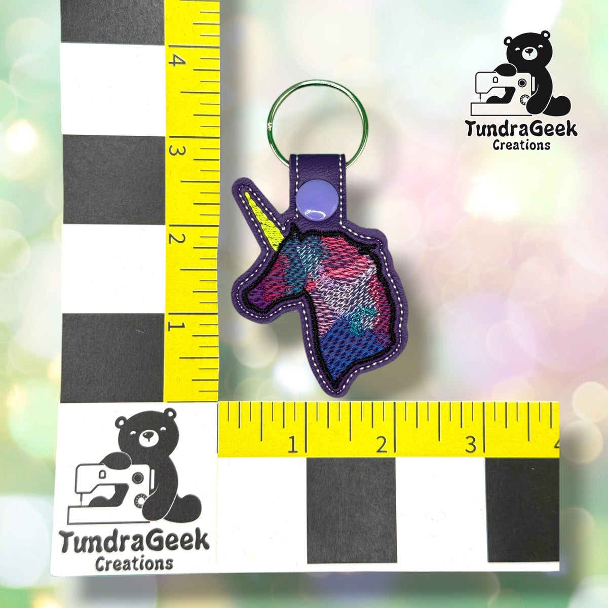 Keychain shown against a black-and-white checkered background with yellow rulers for scale, measuring approximately 3.75 inches tall by 2.25 inches wide including hardware.