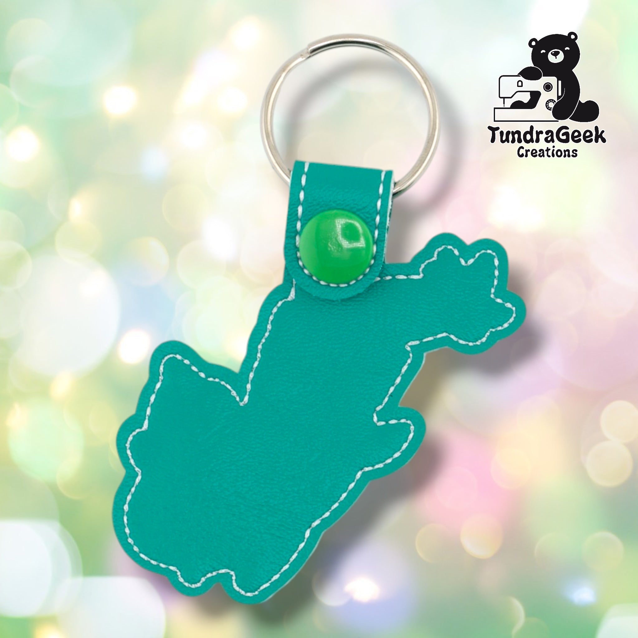 Plain back of the whimsical dragon keychain showing teal faux leather and white outline stitching following the dragon silhouette. Green plastic snap closure at top. No embroidery on reverse.