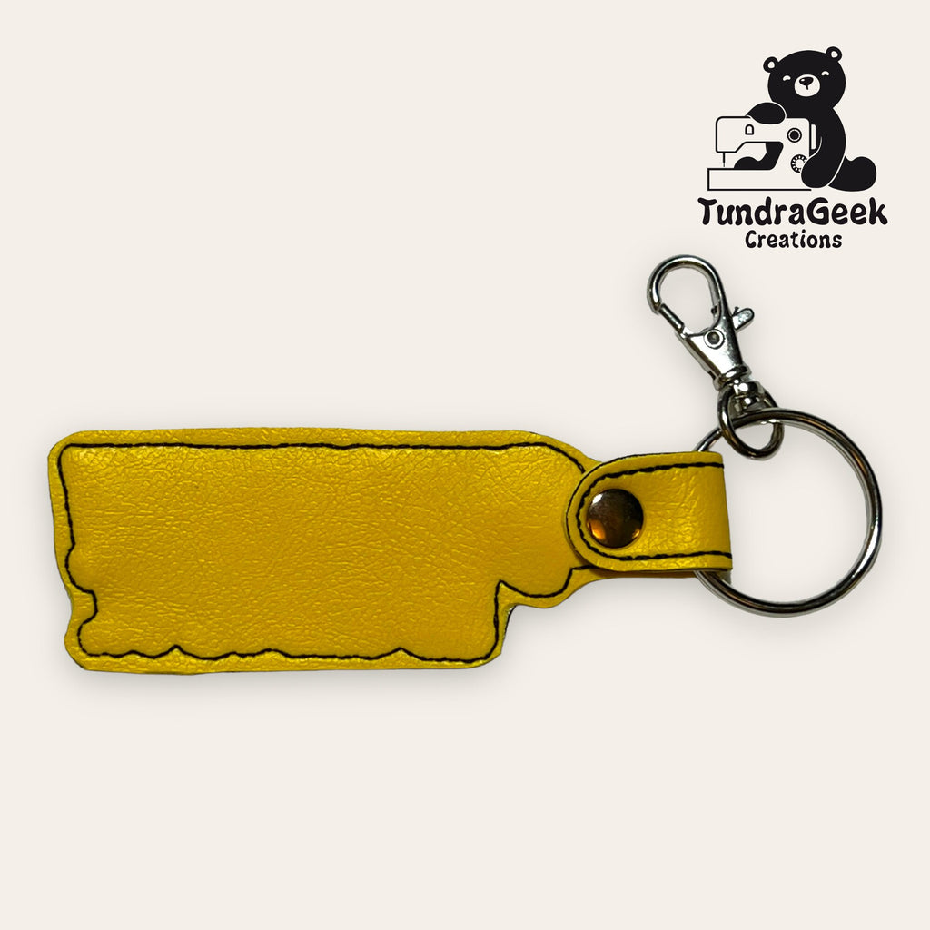 Yellow faux leather keychain in the shape of the state of Oklahoma with a metal ring and clasp, displayed on a plain background with the TundraGeek Creations logo in the corner.