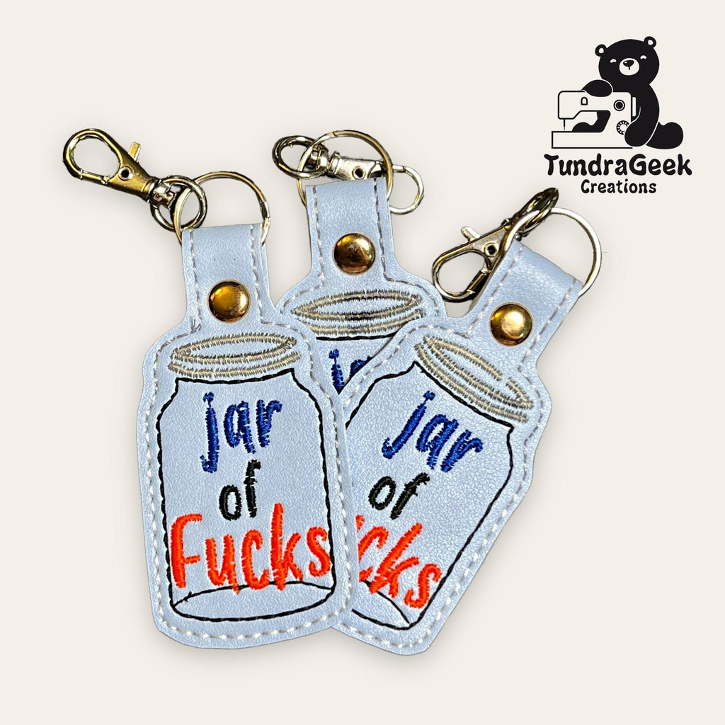 Three embroidered keychains with a jar design and the words jar of fucks displayed, featuring metal clasps. The TundraGeek Creations logo is in the top right corner.