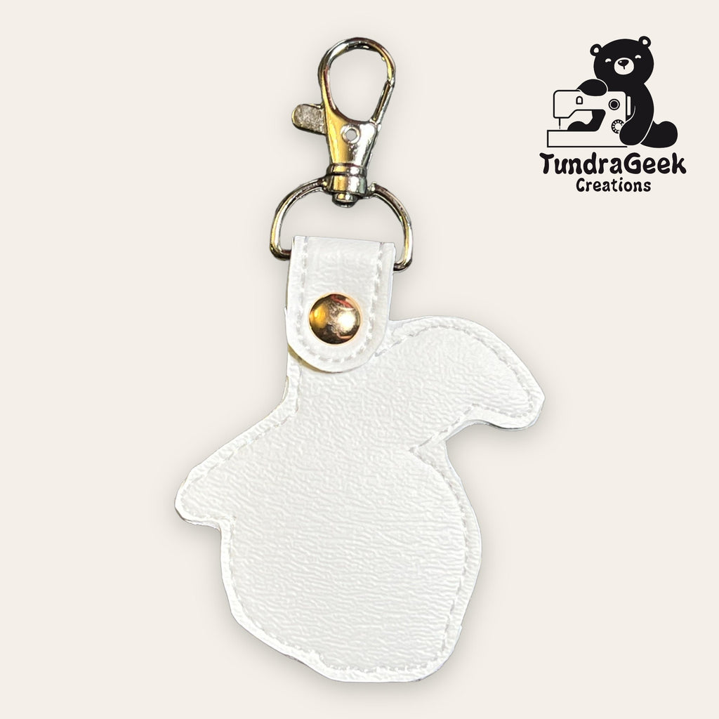 White faux leather rabbit-shaped keychain with a gold snap and clasp, displayed on a plain background with the TundraGeek Creations logo in the top right corner.