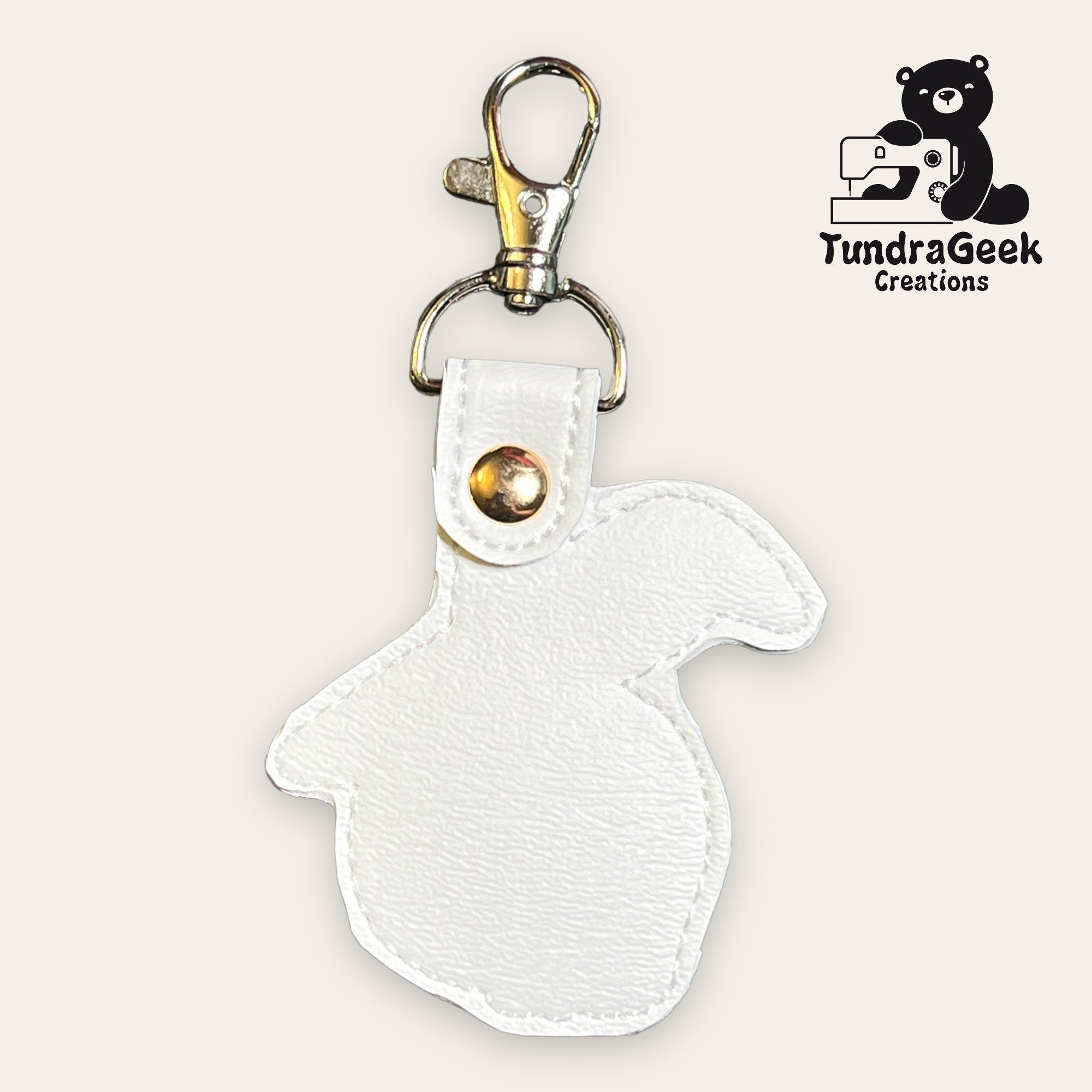 White faux leather rabbit-shaped keychain with a gold snap and clasp, displayed on a plain background with the TundraGeek Creations logo in the top right corner.