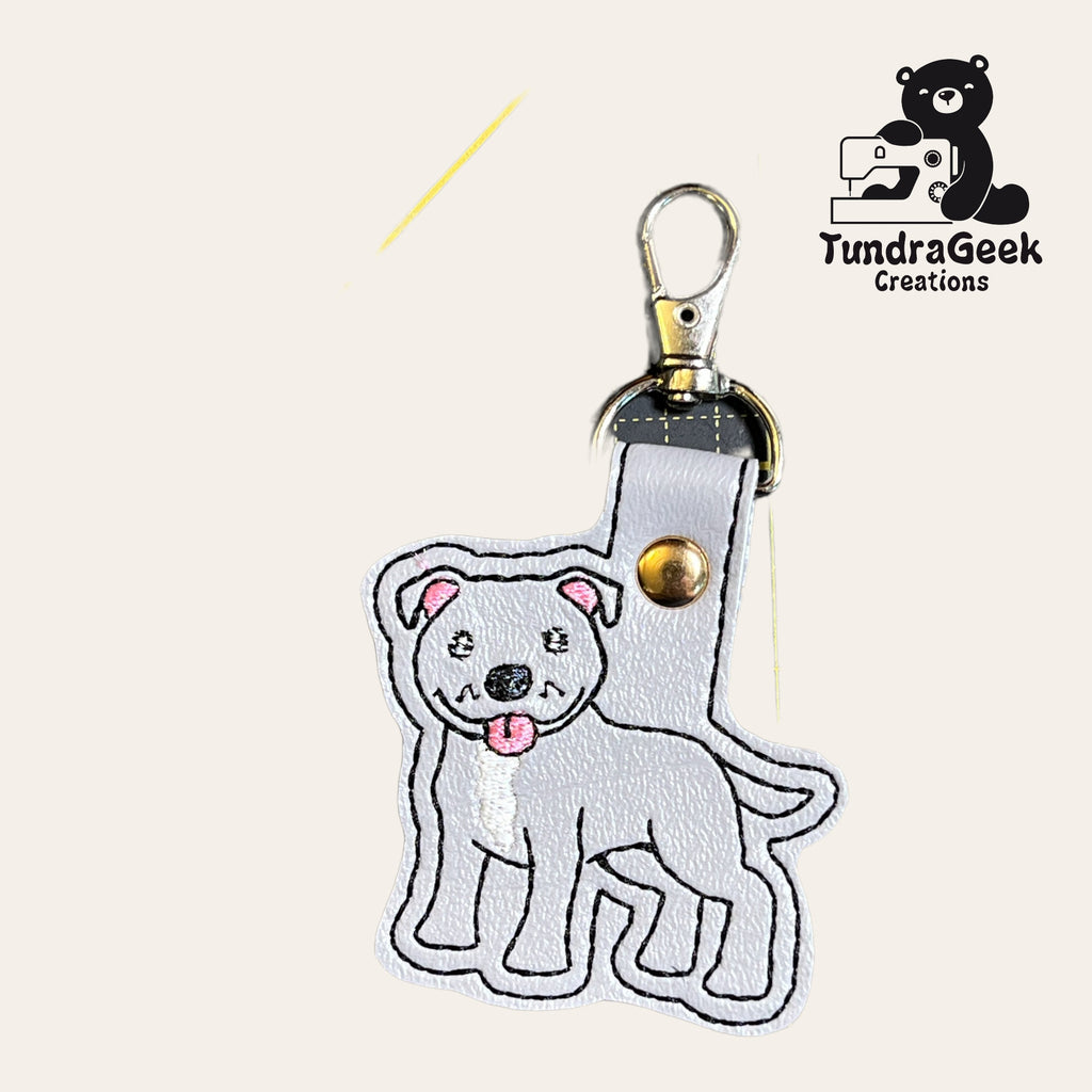 A gray dog keychain with embroidered details, attached to a metal clasp. Logo for TundraGeek Creations is in the top right corner.