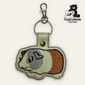 Embroidered guinea pig keychain made of faux leather, attached to a metal keyring with a clasp. TundraGeek Creations logo featuring a bear with a sewing machine is in the top right corner.