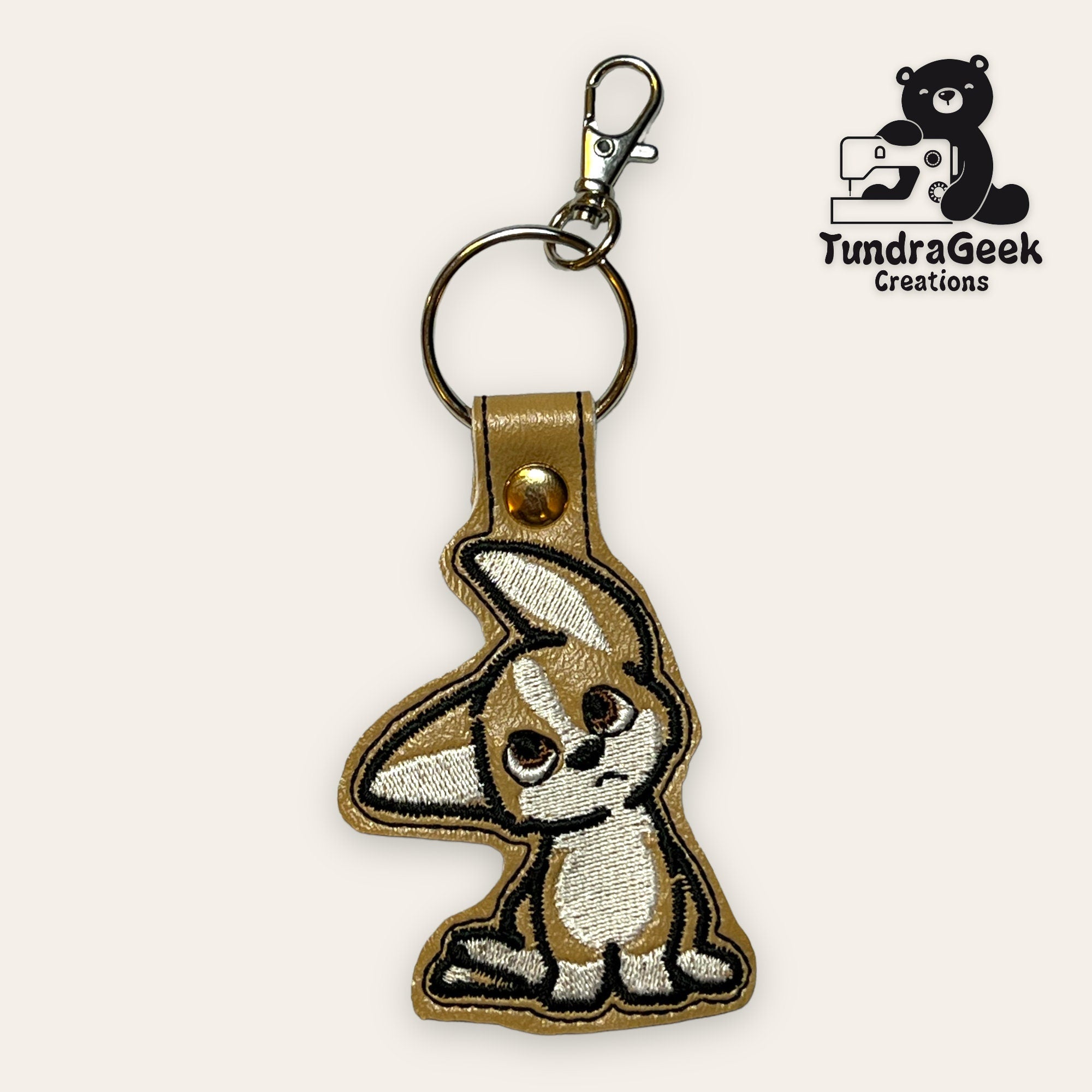Embroidered keychain featuring a cartoon fennec fox with large ears, attached to a metal keyring and clasp. Logo TundraGeek Creations with a bear and sewing machine in the corner.