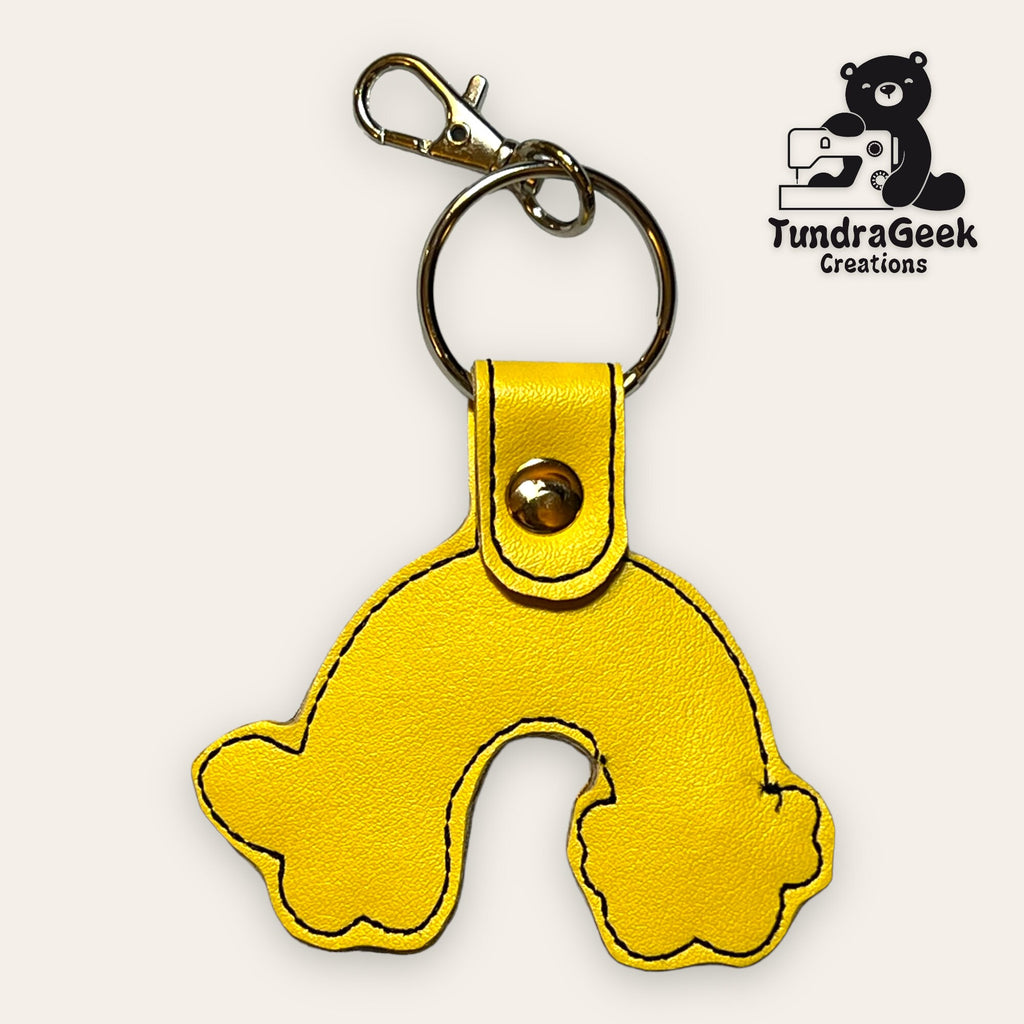 Yellow leather keychain shaped like a stylized animal paw print, with a metal key ring and clasp. TundraGeek Creations logo is in the top right corner.