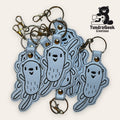 A pile of embroidered keychains shaped like smiling cartoon bacteria, with metal rings and clips. TundraGeek Creations logo is in the top right corner.