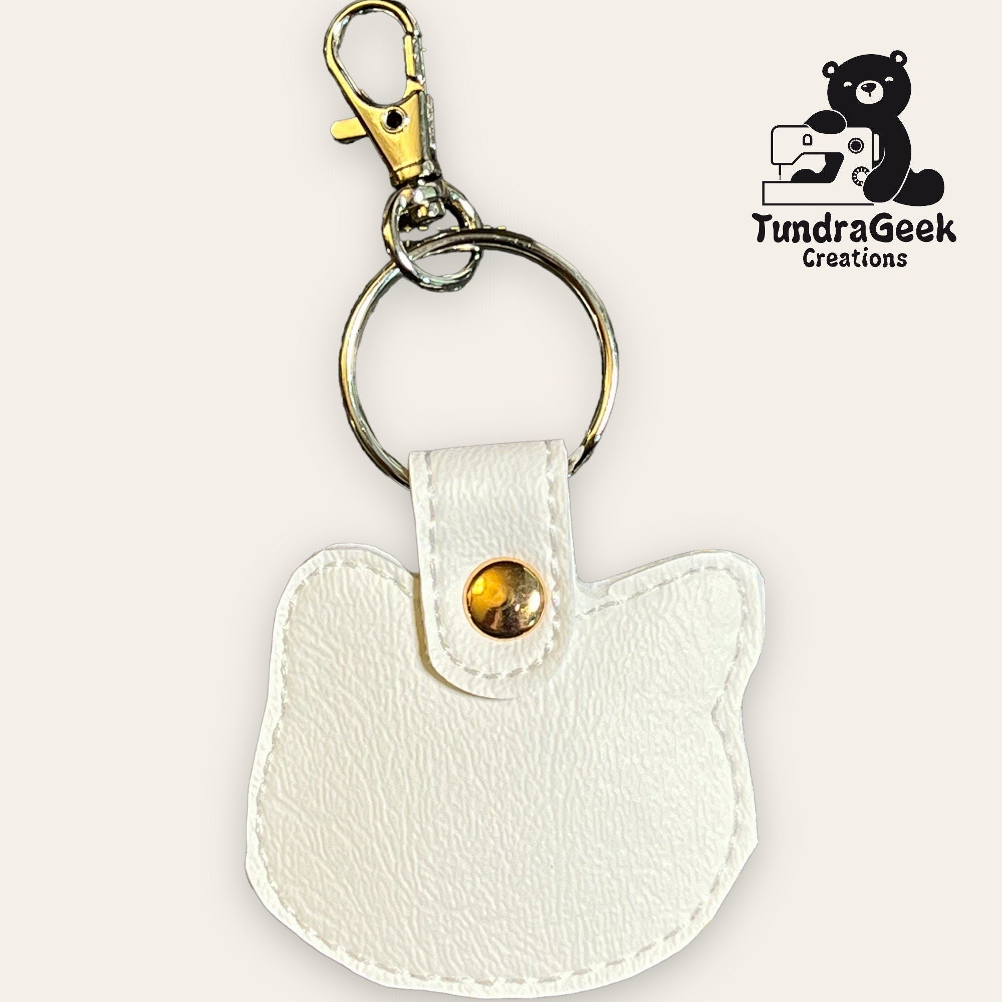 White cat-shaped faux leather keychain with gold snap and metal clip, displayed on a light background with the TundraGeek Creations logo in the corner.