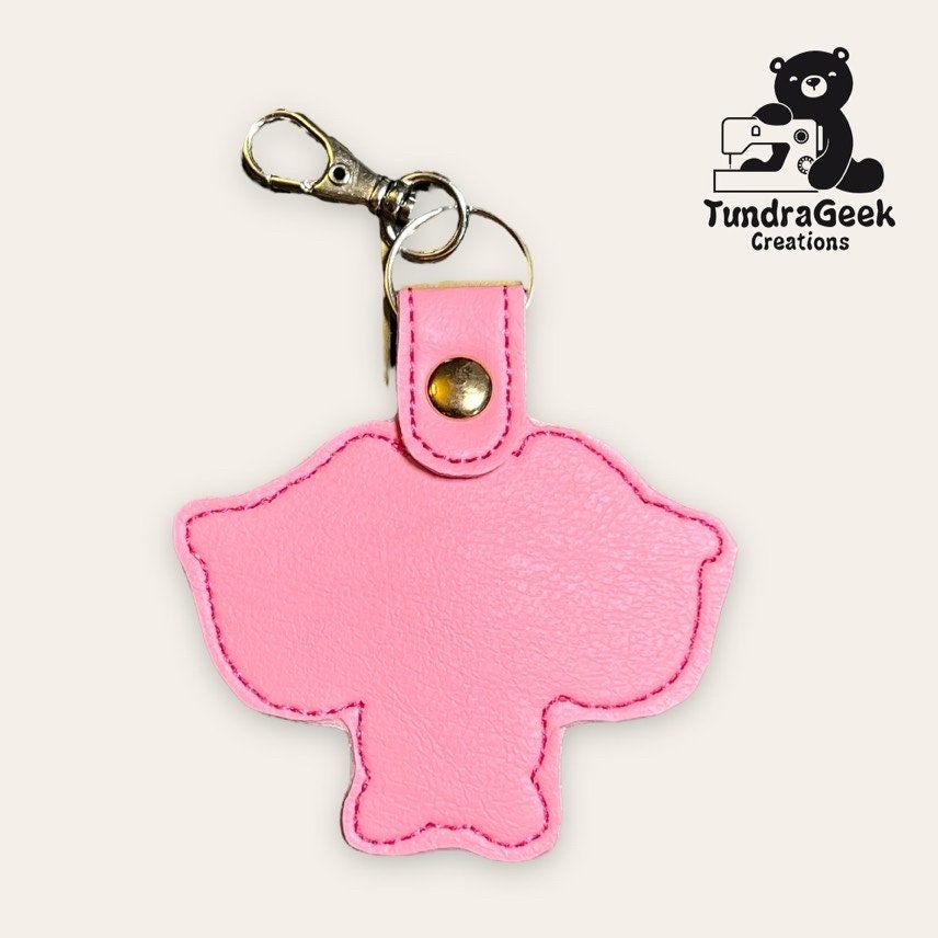 A pink, elephant-shaped faux leather keychain with a metal clip, displayed on a light background. TundraGeek Creations logo is in the top right corner.