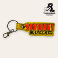 Yellow keychain with the text SHHH! No one cares in red and black, attached to a metal keyring and clasp. TundraGeek Creations logo with a bear and a sewing machine in the top right corner.