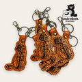 A group of orange, cat-shaped keychains with geometric black stitching, metal key rings, and lobster clasps, displayed on a light background with the TumdraGeek Creations logo.