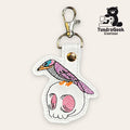 Embroidered keychain with a bird perched on a skull, attached to a metal clasp, with the TundraGeek Creations logo in the corner.