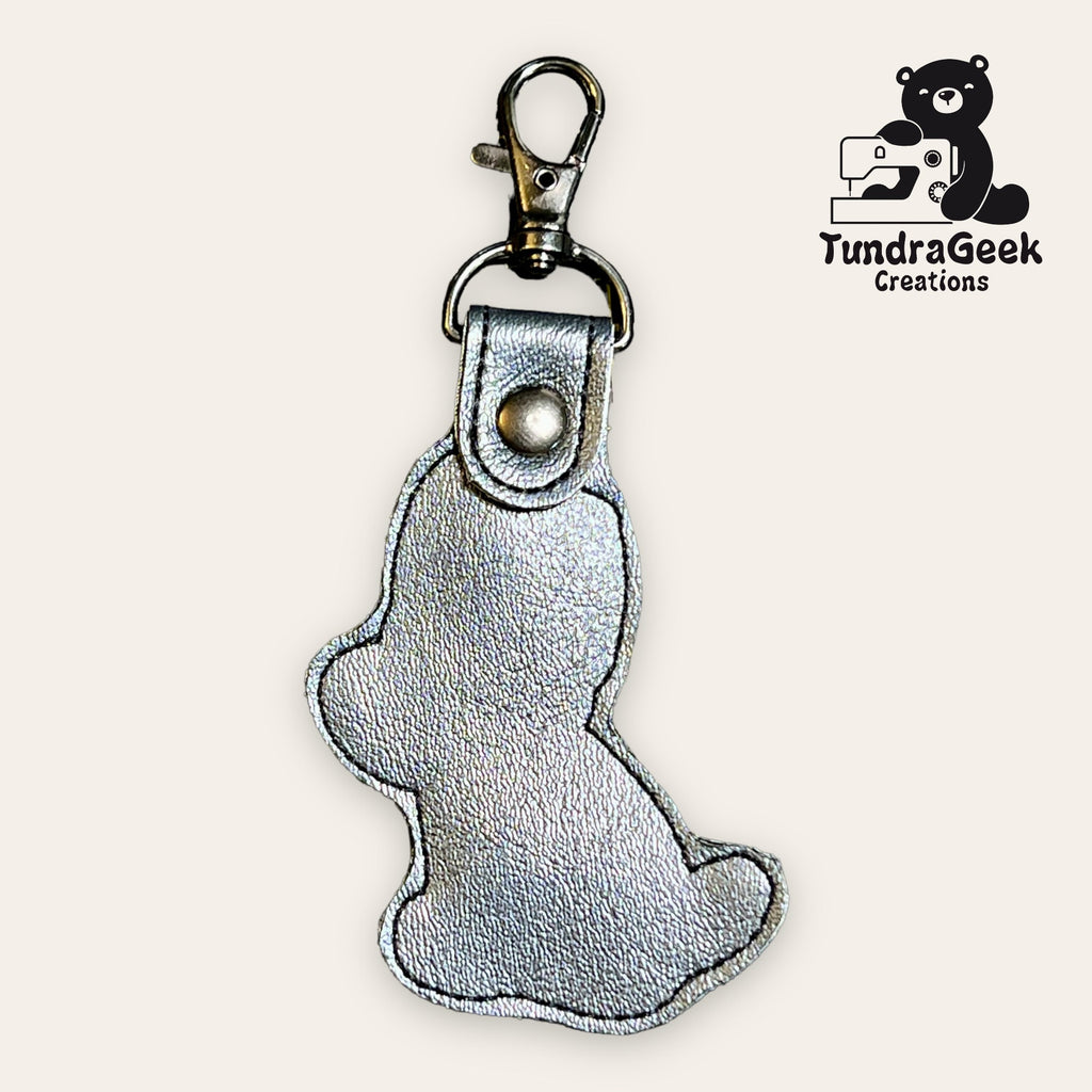 Silver bear-shaped keychain with a metal clasp, displayed on a light background. TundraGeek Creations logo appears in the upper right corner.