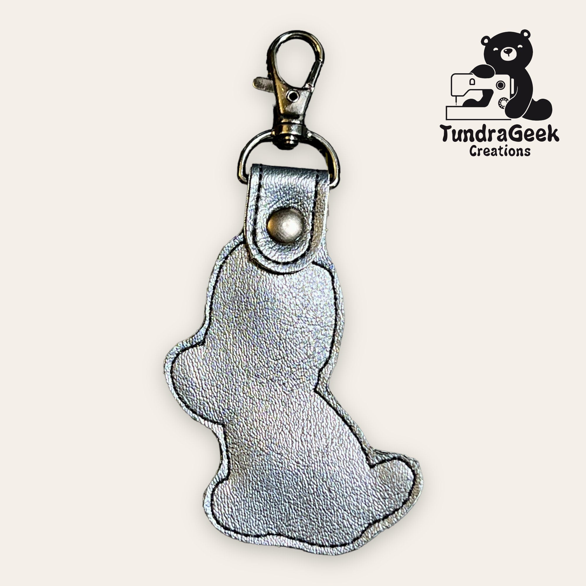 Silver bear-shaped keychain with a metal clasp, displayed on a light background. TundraGeek Creations logo appears in the upper right corner.