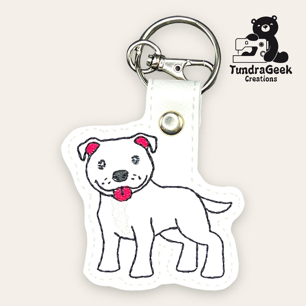 White keychain featuring an embroidered cartoon dog with a red collar, displayed on a white background with the TundraGeek Creations logo in the corner.