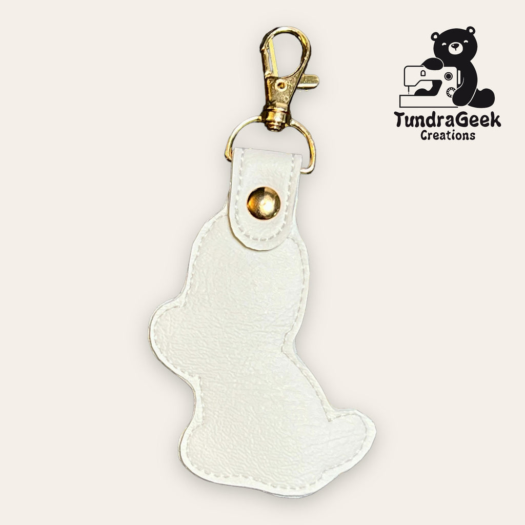A white faux leather bear-shaped keychain with a gold clasp. The TundraGeek Creations logo featuring a bear and sewing machine is in the top right corner.