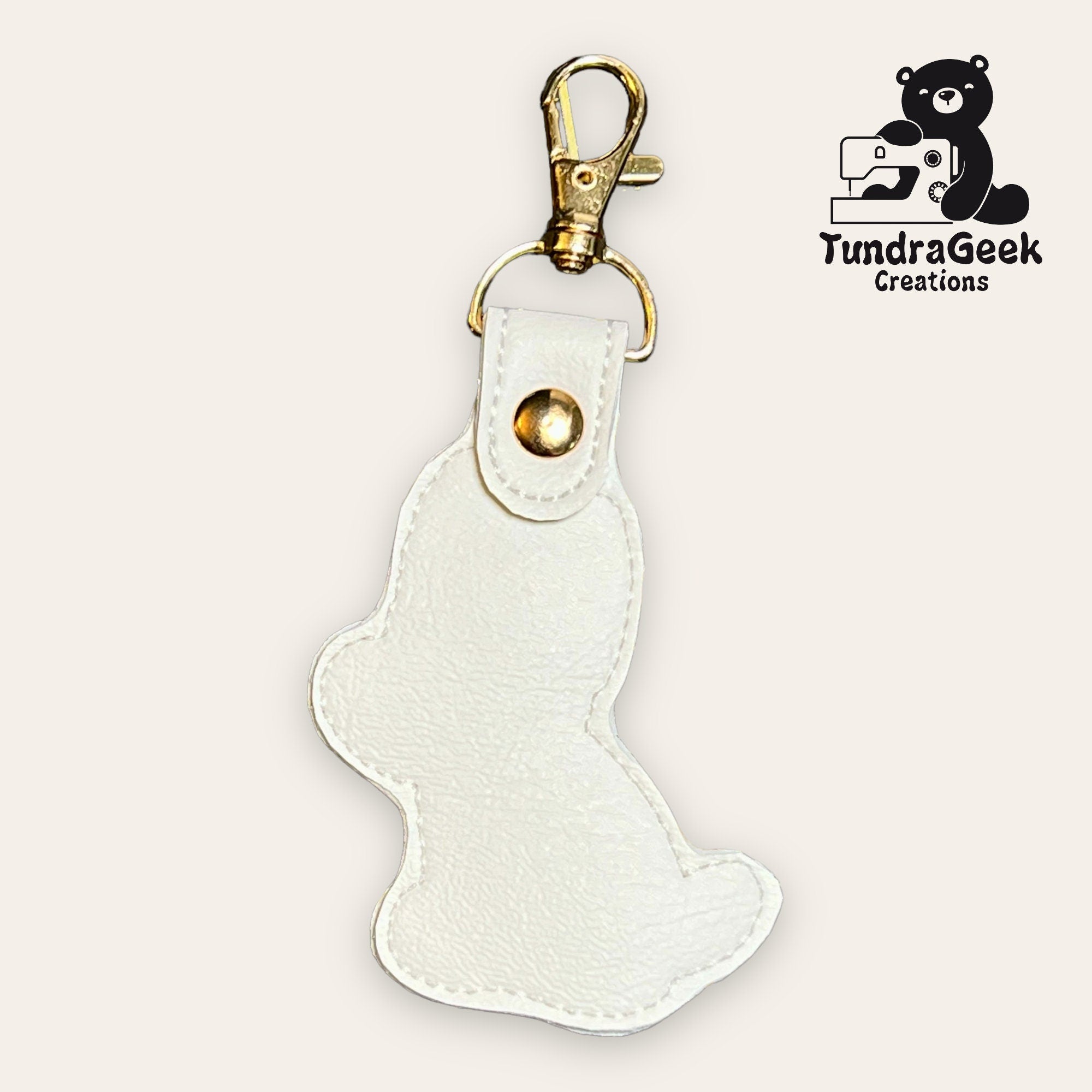 A white faux leather bear-shaped keychain with a gold clasp. The TundraGeek Creations logo featuring a bear and sewing machine is in the top right corner.