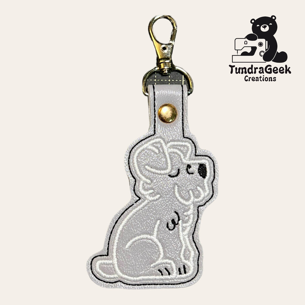 A gray embroidered keychain in the shape of a sitting koala, with a metal clasp. TundraGeek Creations logo featuring a bear and sewing machine is in the upper right corner.