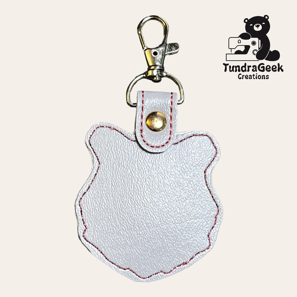 White faux leather keychain in the shape of a bears head with pink stitching and a metal clasp, displayed next to the TundraGeek Creations logo.