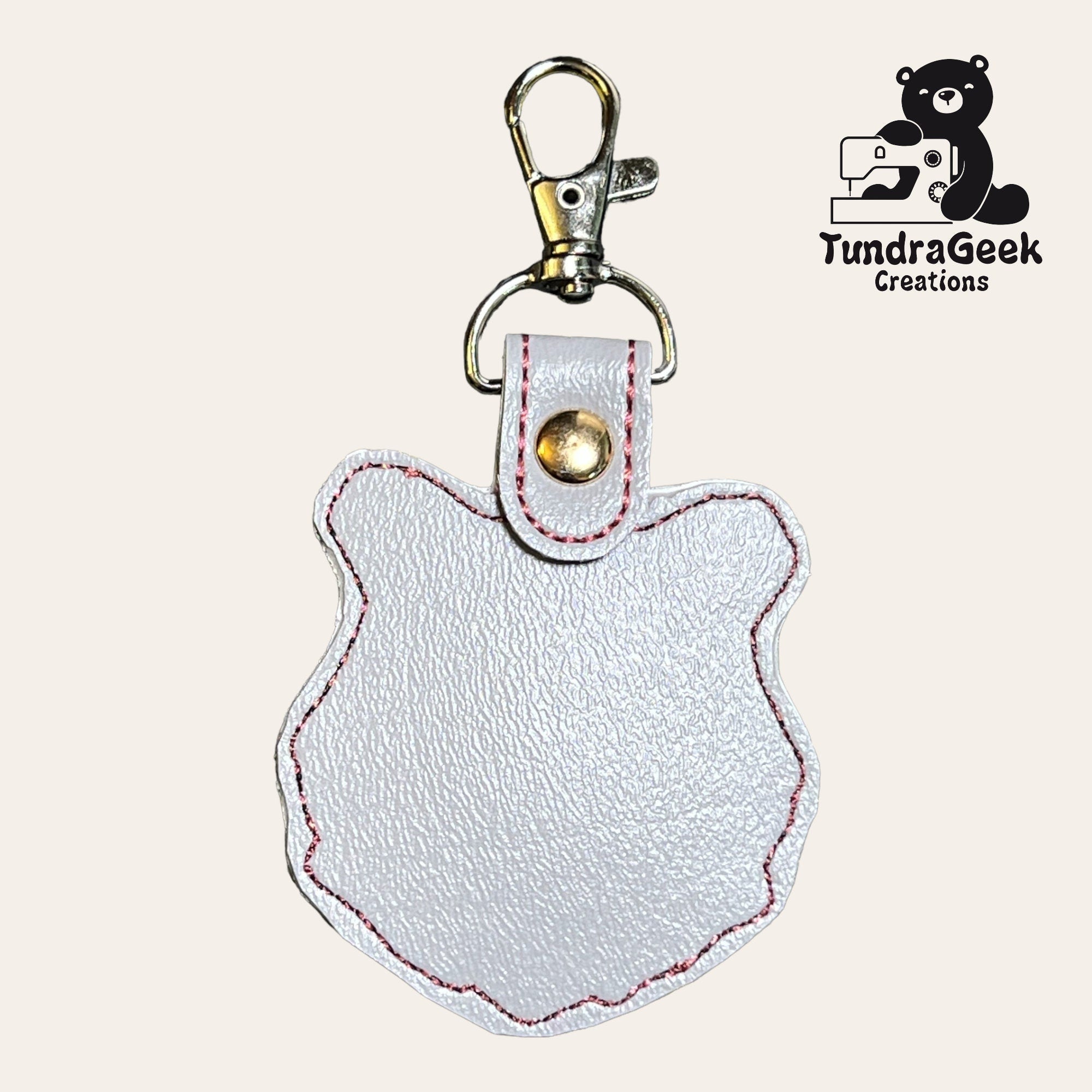 White faux leather keychain in the shape of a bears head with pink stitching and a metal clasp, displayed next to the TundraGeek Creations logo.