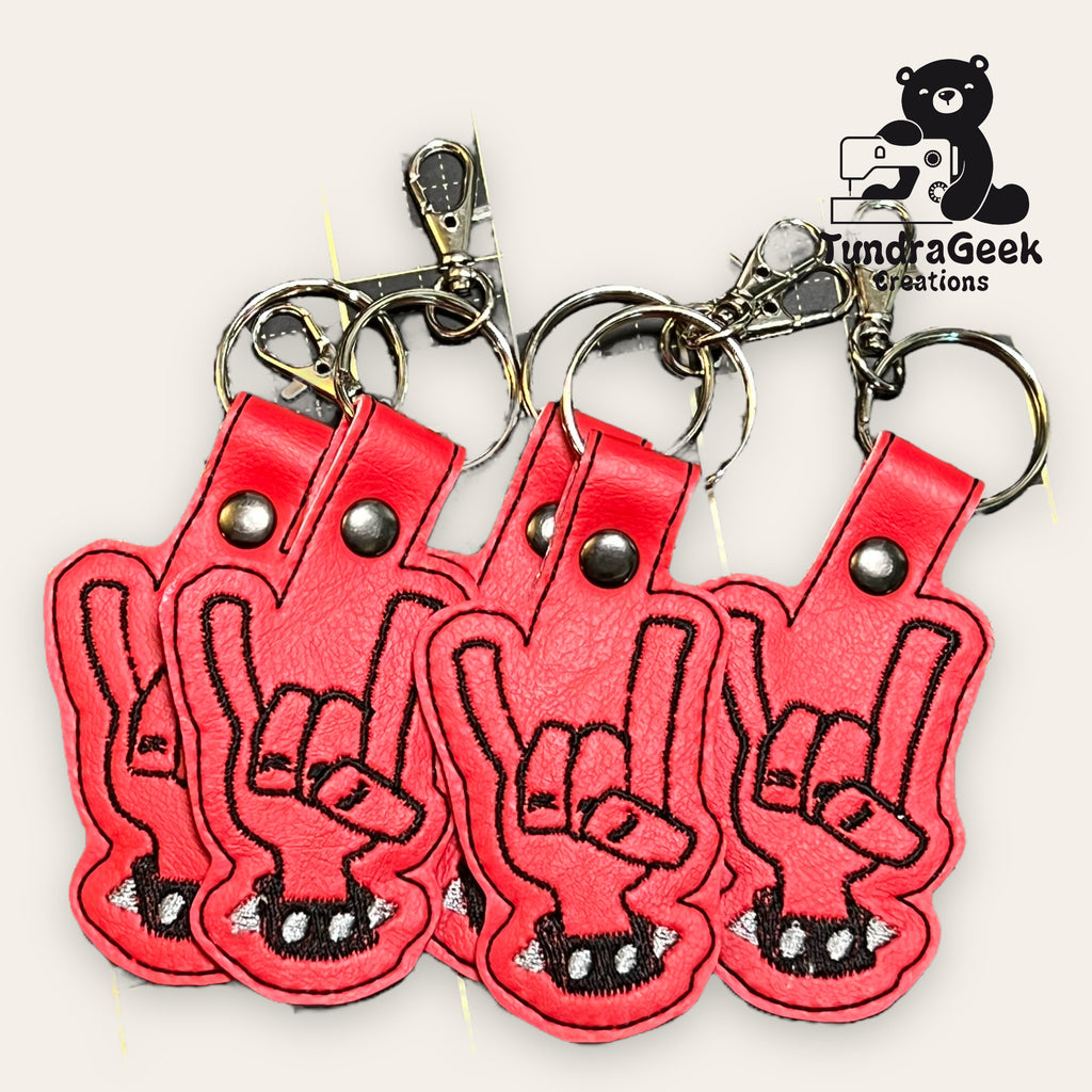 Four red keychains shaped like hands making the rock on gesture are displayed on a light background with the TundraGeek Creations logo in the corner.