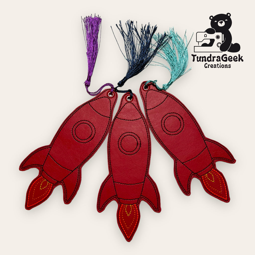 Three red rocket-shaped keychains with colorful tassels are arranged side by side. The TundraGeek Creations logo appears in the top right corner.