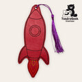 Red rocket-shaped faux leather bookmark with stitched details and a purple tassel, displayed next to the TundraGeek Creations logo featuring a bear holding a sewing machine.