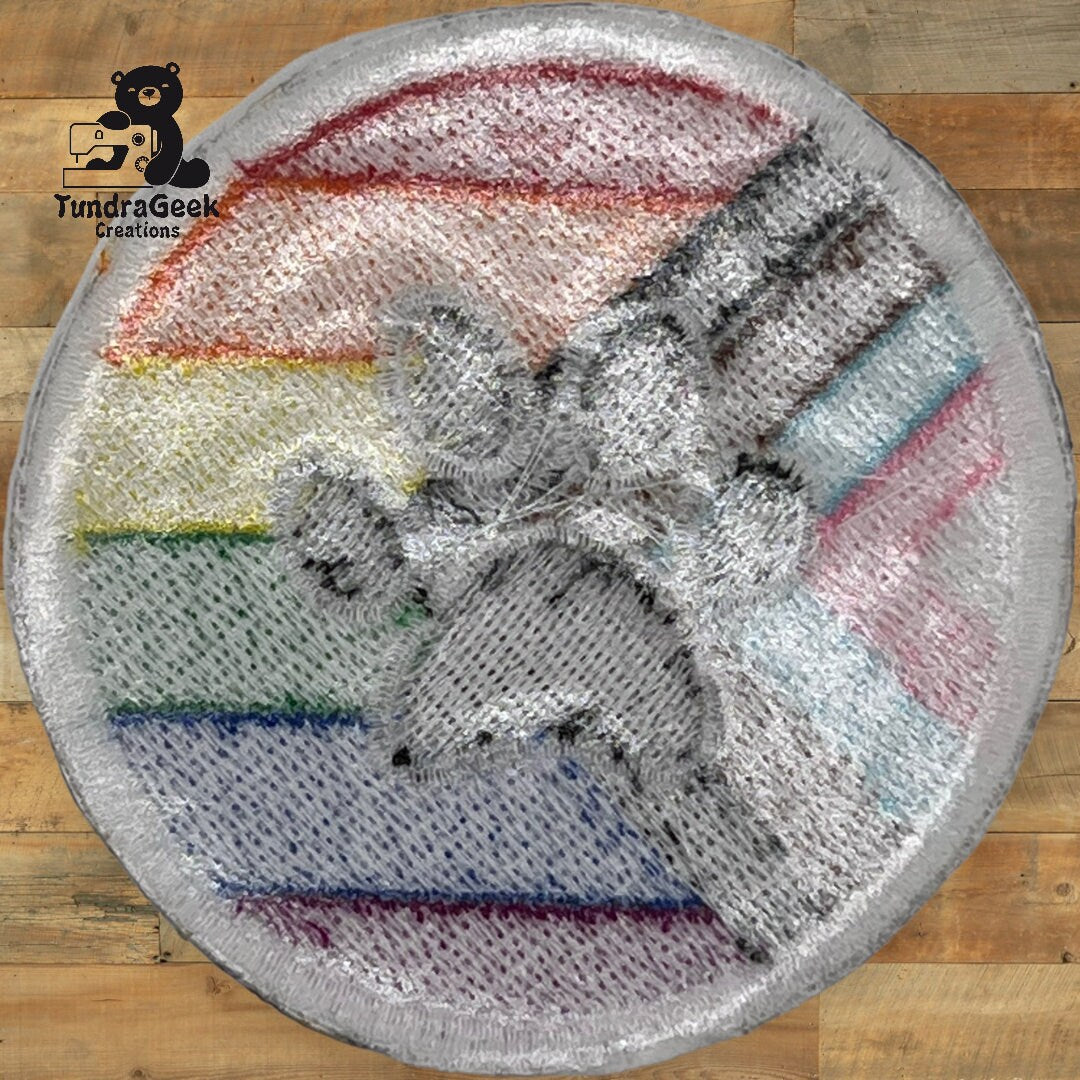 A round rug with a rainbow-striped background and a large gray paw print design, photographed on a wooden floor. Logo TundraGeek Creations is in the top left corner.