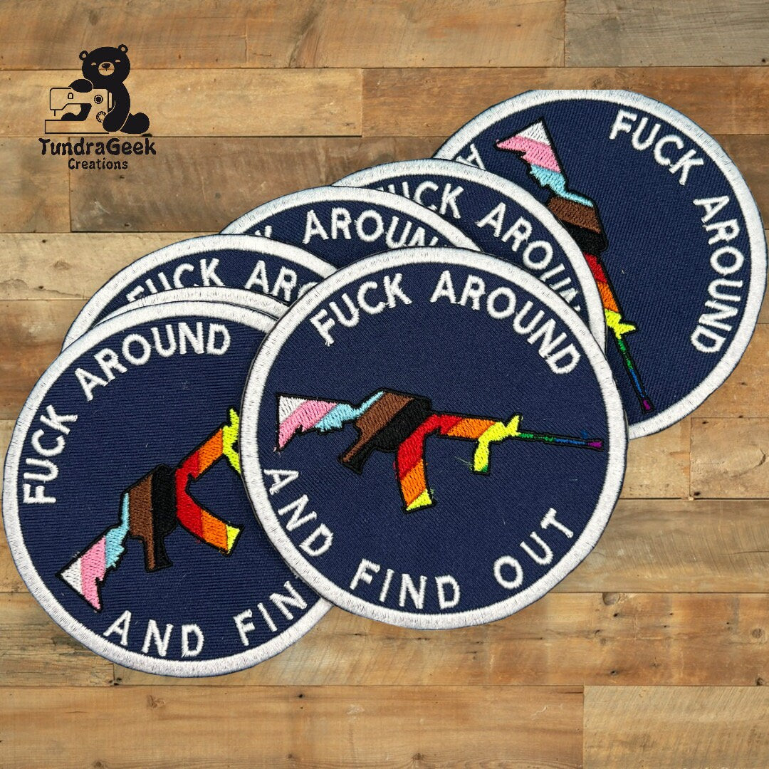 Four round patches on a wooden surface, each showing a colorful rifle and the words FUCK AROUND AND FIND OUT embroidered in white text.