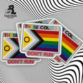 Three rectangular patches display the Progress Pride flag and the words THESE COLORS DONT RUN on a black and white wavy optical illusion background.