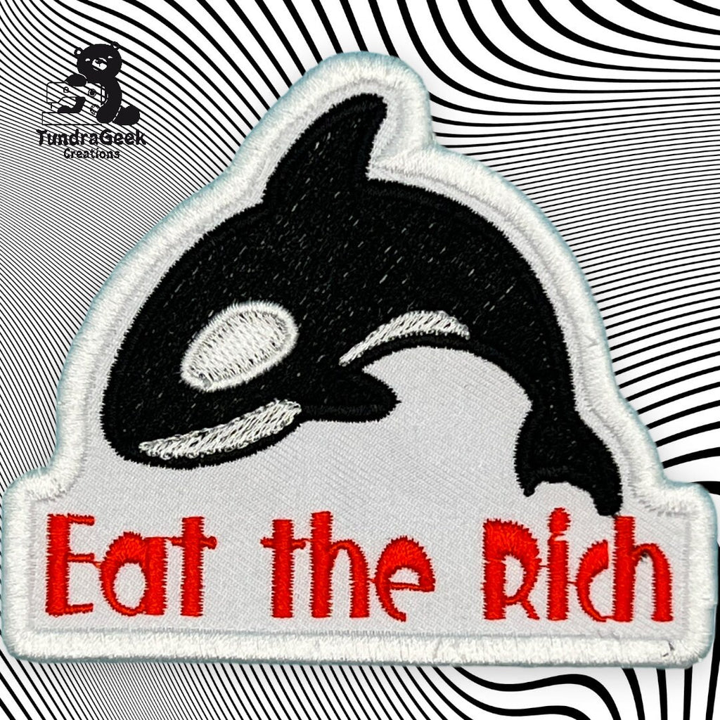 Embroidered patch of an orca with the text Eat the Rich in red, set against a black and white swirling background.