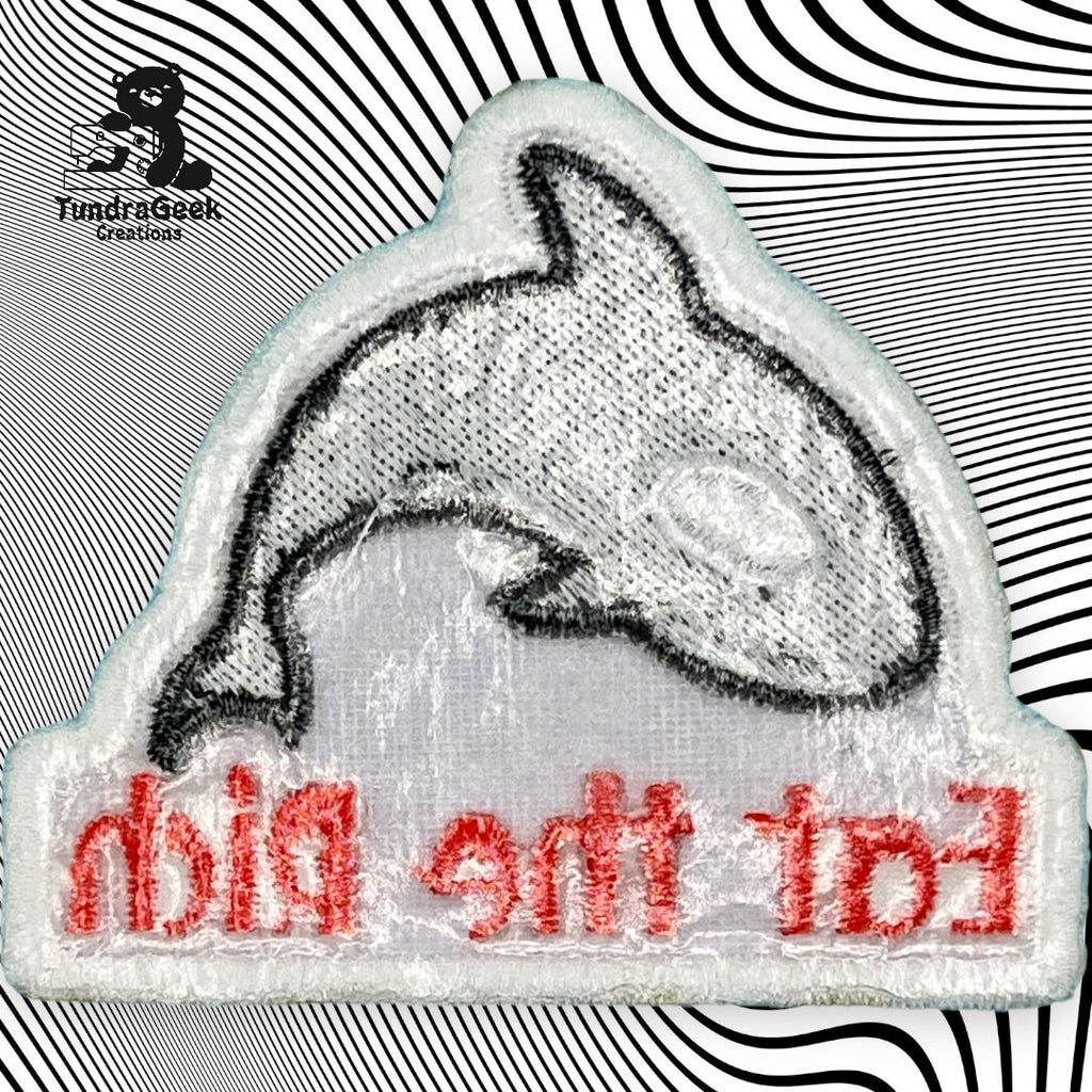 A patch with a black and white outline of a whale and red text reading Eat The Rich in reverse, placed on a black and white wavy background.