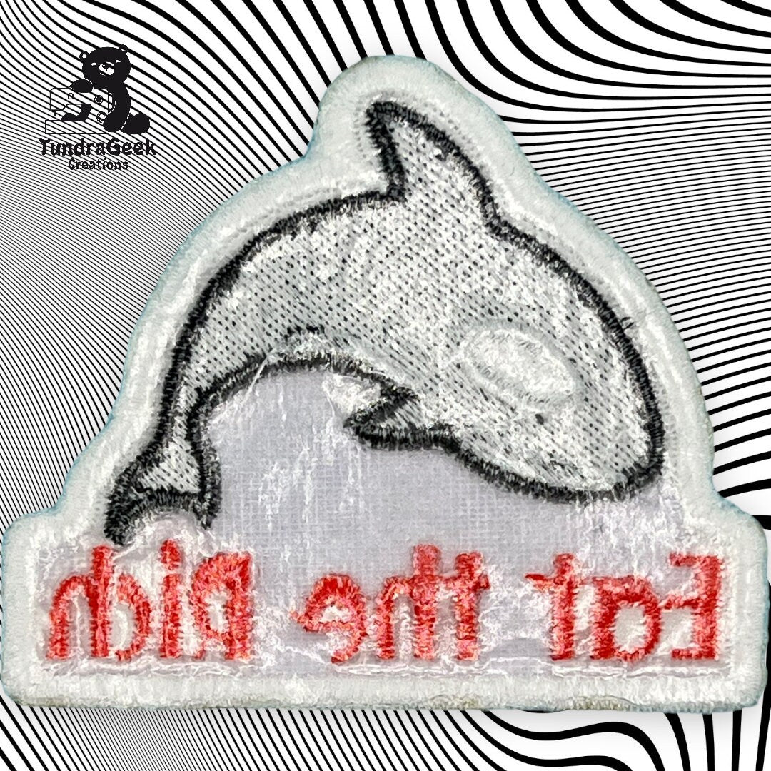 A patch with a black and white outline of a whale and red text reading Eat The Rich in reverse, placed on a black and white wavy background.