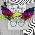 A pair of rainbow-colored, skull-shaped shoe accessories are displayed on a card with a sneaker illustration and lime green laces, set against a black-and-white swirling pattern background.