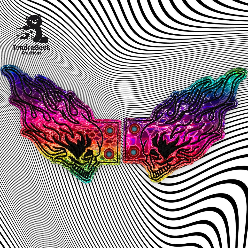 A pair of rainbow-colored, wing-shaped belt buckles on a black and white wavy striped background with the FundrGeek Creations logo in the corner.