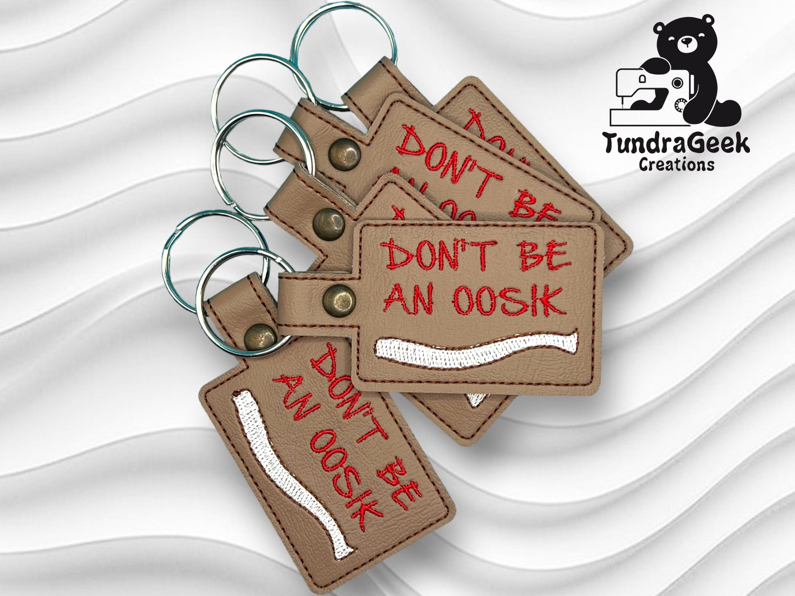 Four brown rectangular keychains with red embroidered text DONT BE AN OOSIK and a white bone graphic, displayed with the TundraGeek Creations logo in the corner.