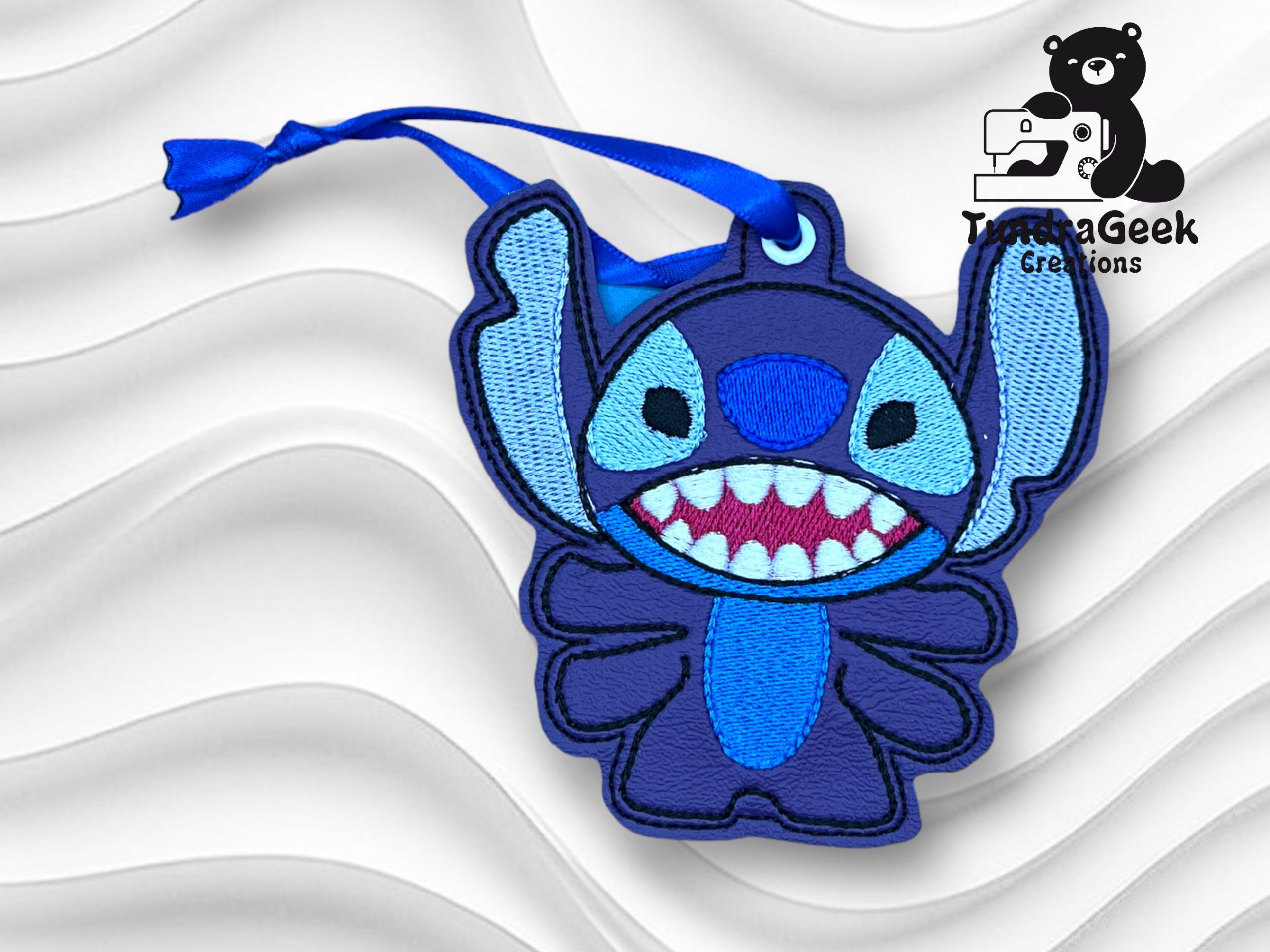 Blue embroidered keychain of Stitch from Disney’s Lilo & Stitch with a blue ribbon, displayed on a wavy white background with the TurtleaGeek Creations logo in the corner.
