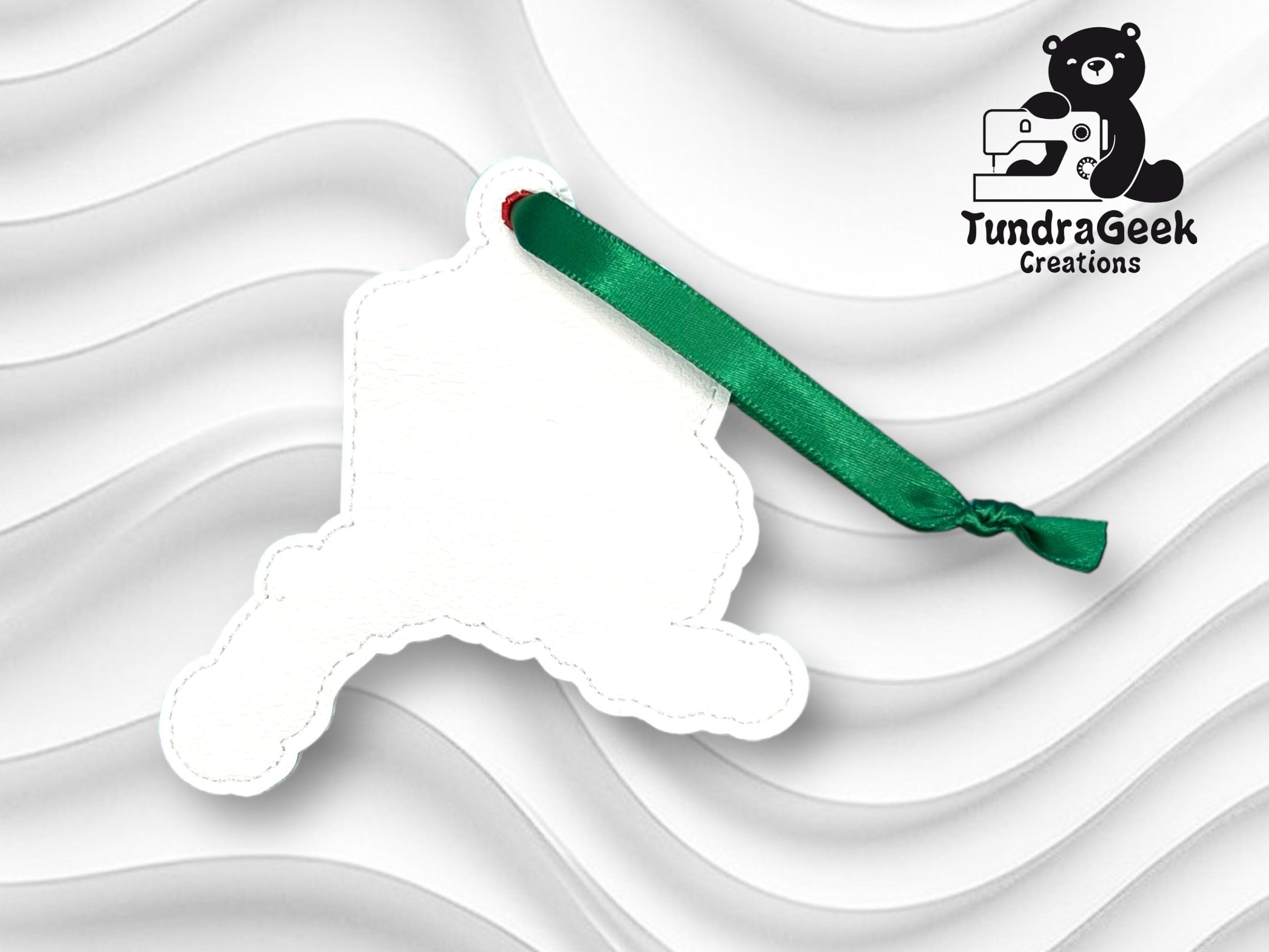 A white, silhouette-shaped ornament with a green ribbon is displayed on a wavy white background, featuring the TundraGeek Creations logo in the top right corner.