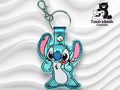 Embroidered blue cartoon character keychain with pink ears and a metal clip, displayed on a wavy white background. The logo TundraGeek Creations appears in the top right corner.