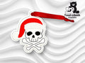 A skull and crossbones wearing a red Santa hat, embroidered keychain with a red ribbon, displayed on a wavy white background. TundraGeek Creations logo in the top right corner.
