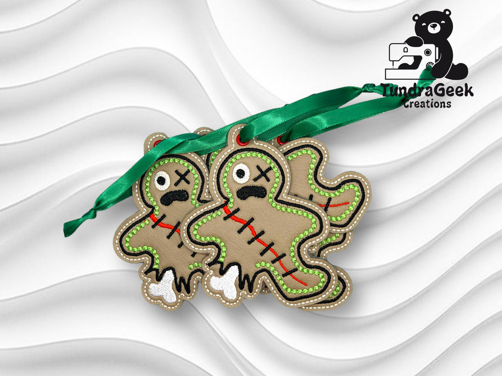 Two gingerbread-shaped ornaments with stitched details and green ribbons, featuring one large eye, red scar lines, and a distressed expression, on a textured white background.