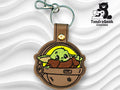 Embroidered keychain featuring a green, cartoonish alien in a brown pod with a metal clasp, displayed on a wavy white background with TundraGeek Creations logo.