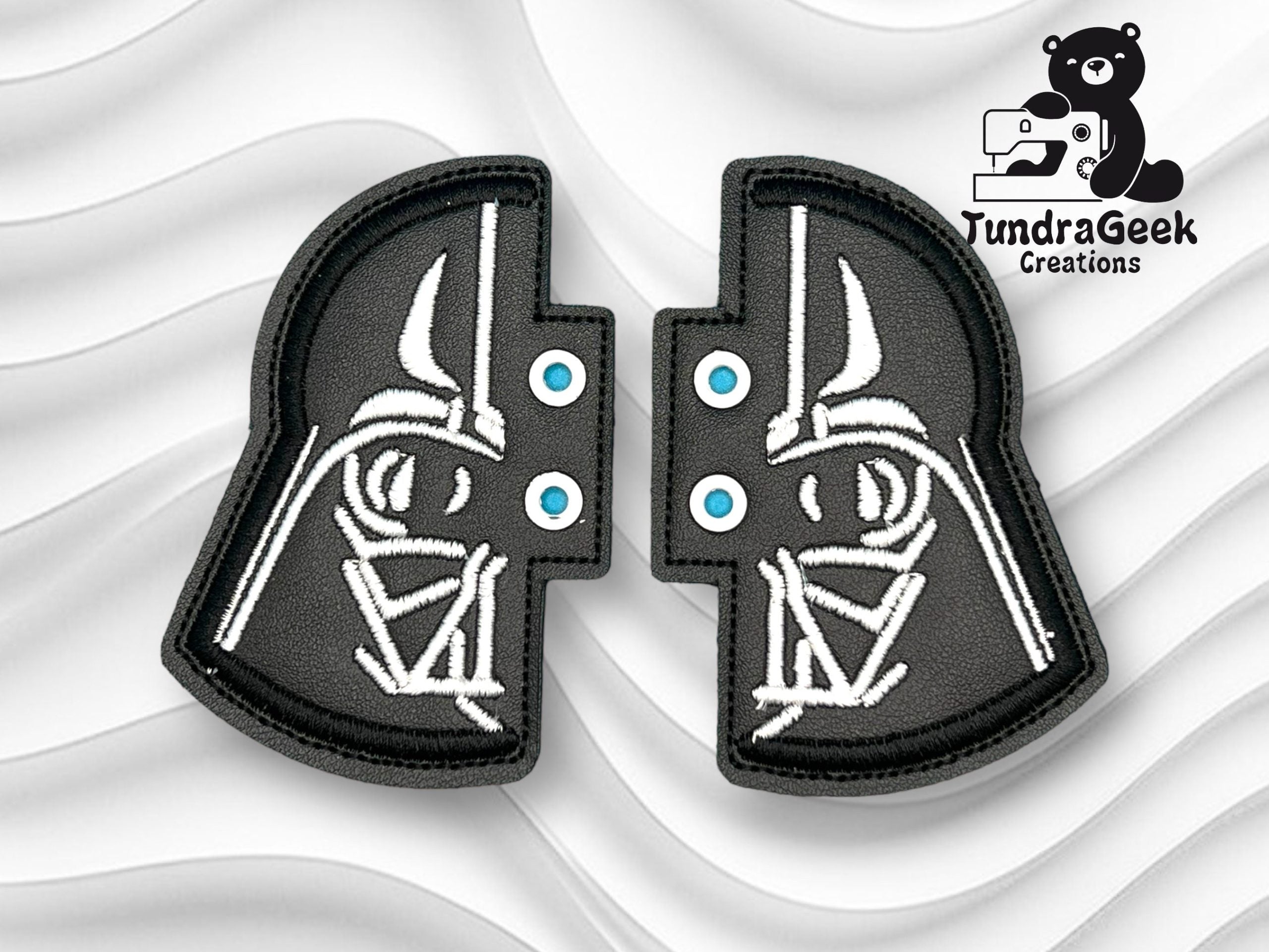 Two black and white embroidered patches form a split Darth Vader helmet design, positioned on a wavy white background with the TundraGeek Creations logo in the top right corner.