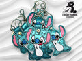 Four embroidered blue cartoon character keychains with pink ears are displayed on a wavy white background, with the TundraGeek Creations logo in the top right corner.