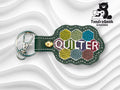 Green leather keychain with QUILTER embroidered in multicolored hexagons, metal clasp attached; TundraGeek Creations bear logo in the top right corner.