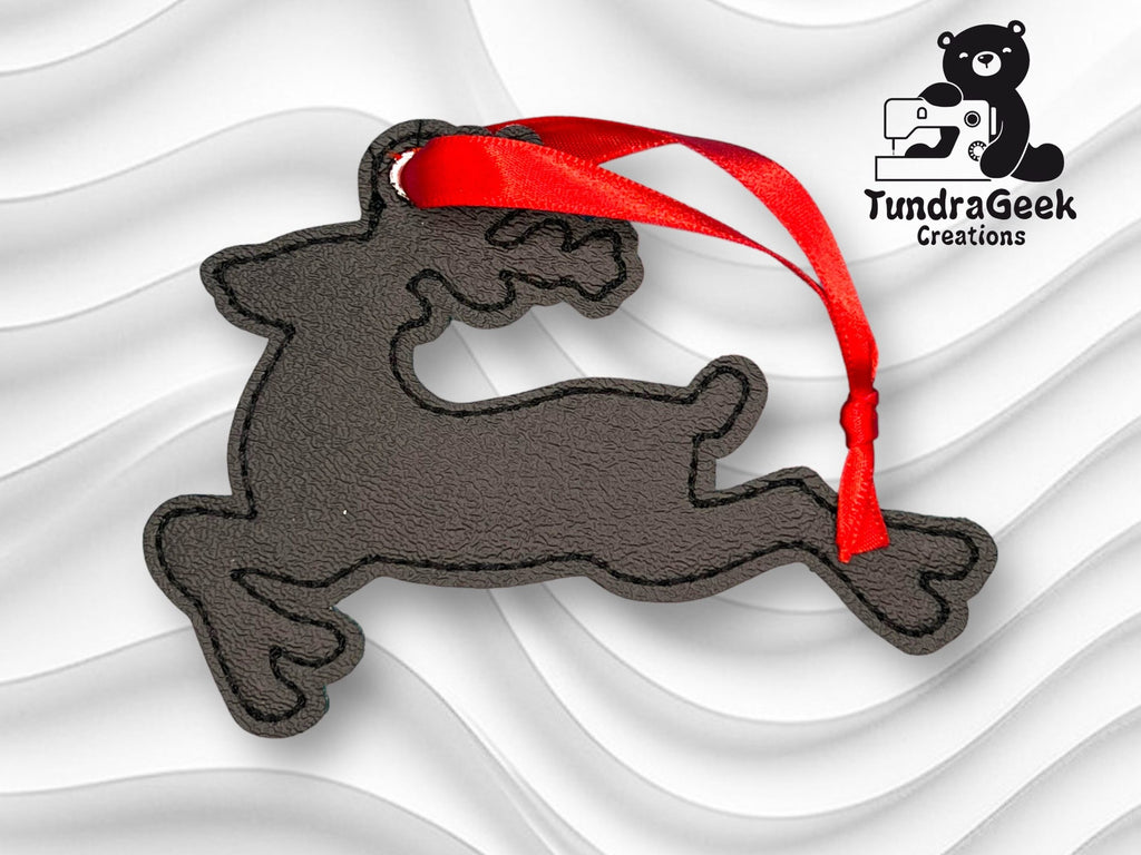 A black reindeer-shaped ornament with a red ribbon lies on a textured white background, with the TundraGeek Creations logo in the top right corner.