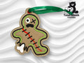 Brown and green patchwork gingerbread man ornament with a green ribbon, featuring stitching details and a cartoonish distressed face. TundraGeek Creations logo in the top right corner.