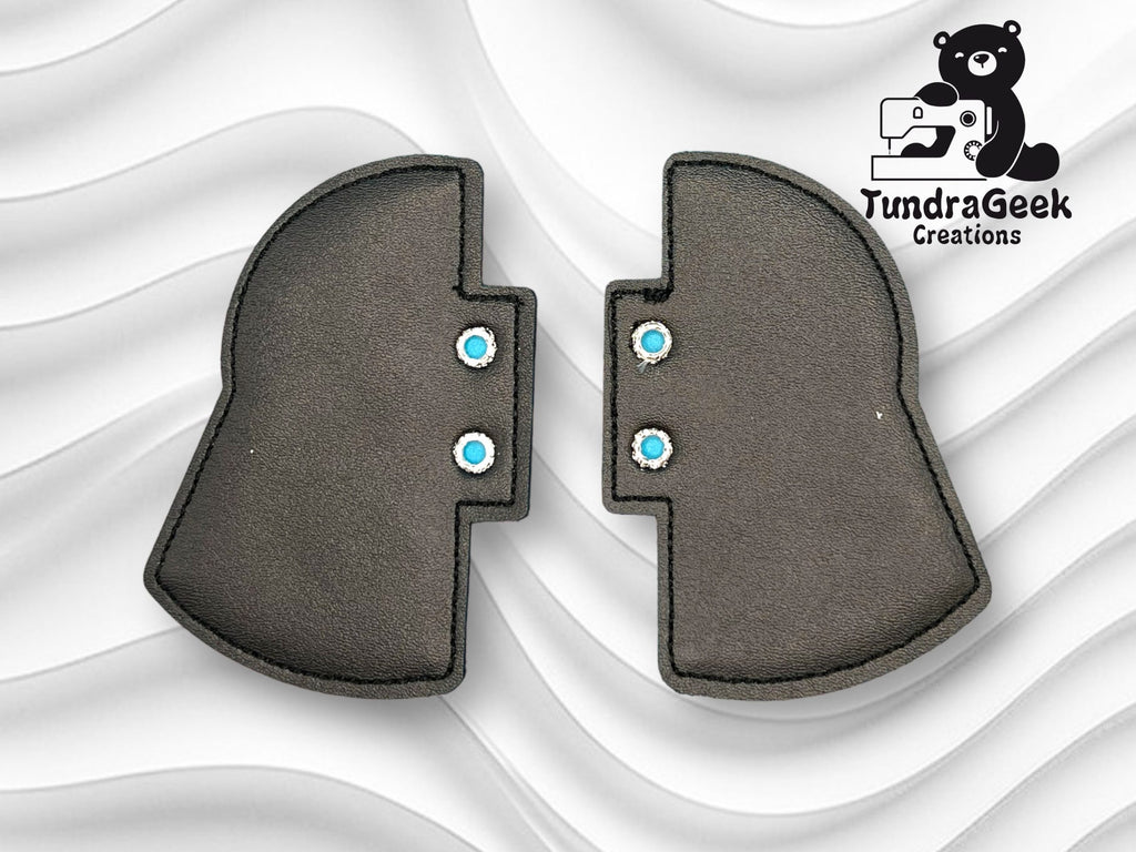Two black, helmet-shaped pieces with blue snaps are placed side by side on a wavy white background. A TundraGeek Creations logo with a bear is in the top right corner.