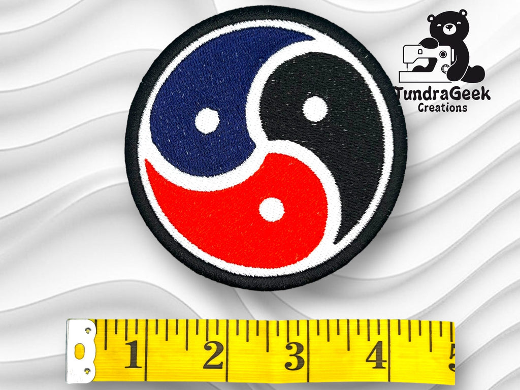 Circular embroidered patch with a blue, red, and black yin-yang-like design, placed above a measuring tape reading about 3 inches; TundraGeek Creations logo in the corner.